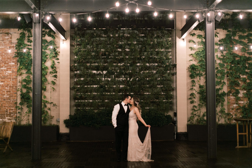 Bride and groom kissing at end of wedding night in front of green wall