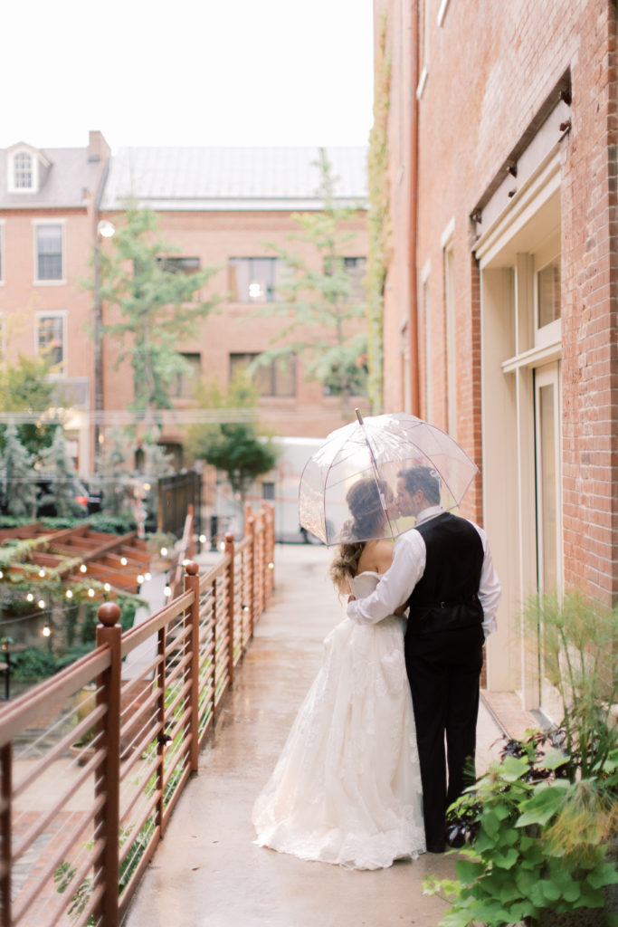 Bride and groom kissing under umbrella on wedding day